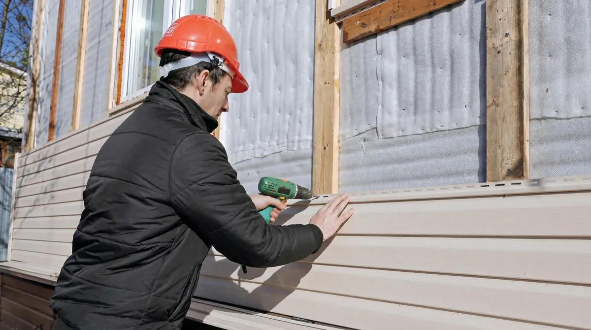 Siding replacement professional using a power drill to install new tan vinyl siding on a home exterior in Indianapolis, IN